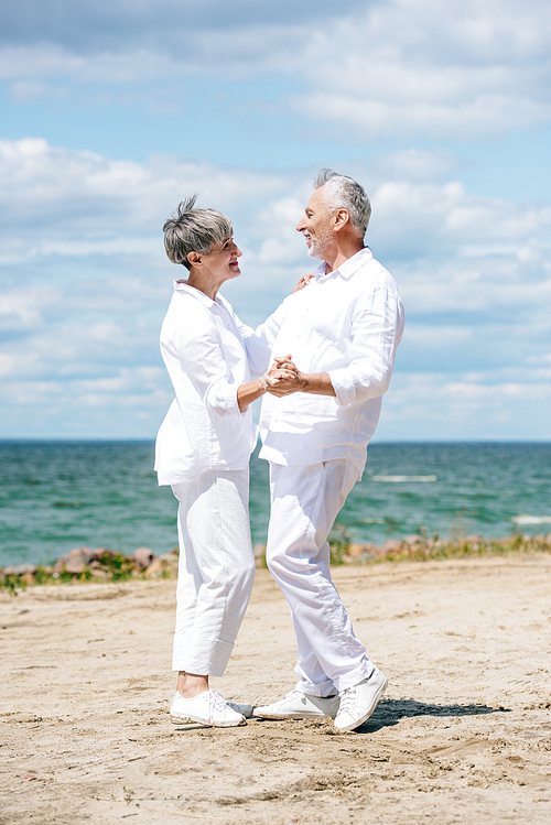 full length view of happy senior couple looking at each other while dancing at beach