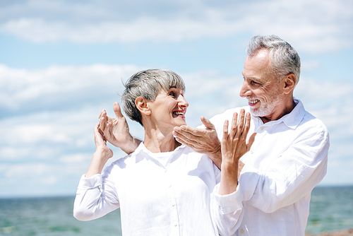 happy senior couple in white shirts standing under blue sky in sunny day