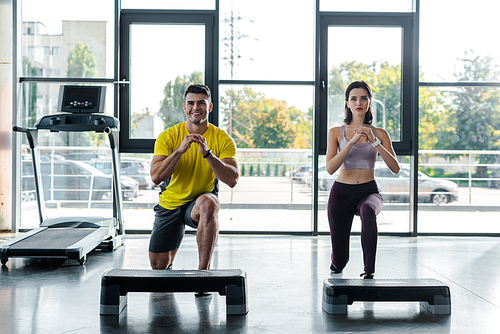 smiling sportsman and sportswoman doing lunges in sports center
