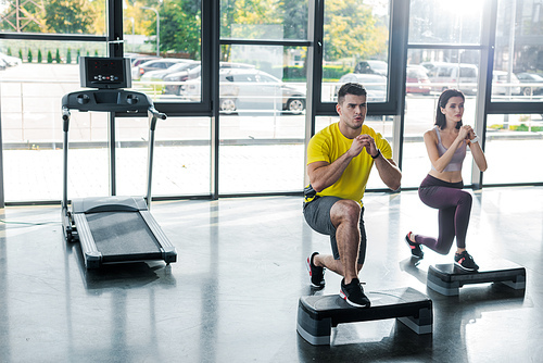 handsome sportsman and sportswoman doing lunges on step platforms in sports center