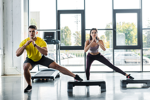handsome sportsman and sportswoman doing lunges on step platforms in sports center