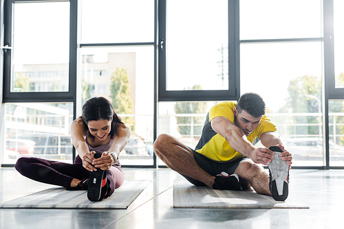 sportsman and sportswoman stretching on fitness mats in sports center