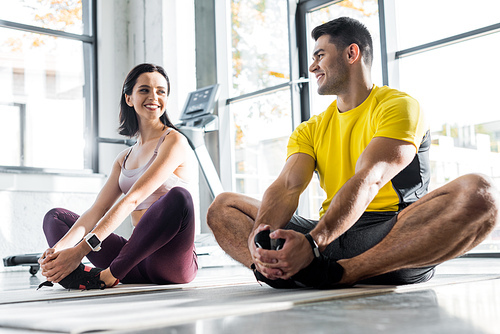 smiling sportsman and sportswoman stretching on fitness mats in sports center