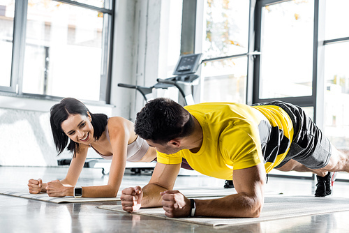 sportsman and smiling sportswoman doing plank on fitness mats in sports center