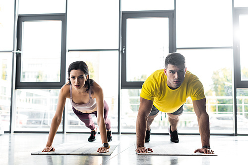 sportsman and sportswoman doing plank on fitness mats in sports center