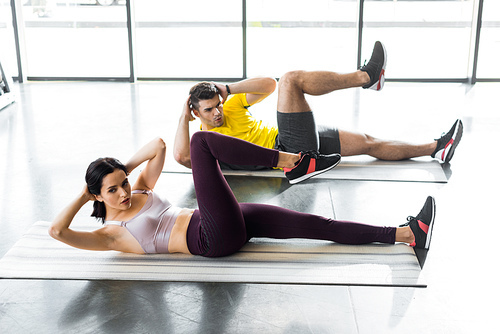 sportsman and sportswoman doing crunches on fitness mats in sports center