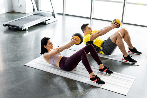 sportsman and sportswoman doing crunches with balls on fitness mats in sports center