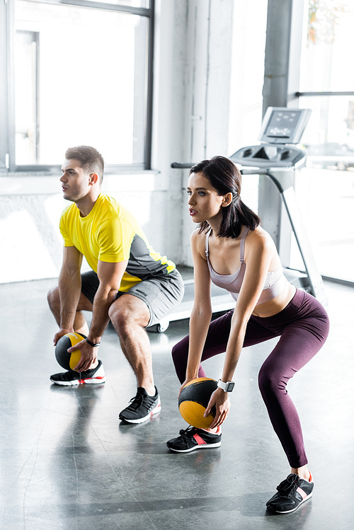 sportsman and sportswoman doing squat with balls in sports center