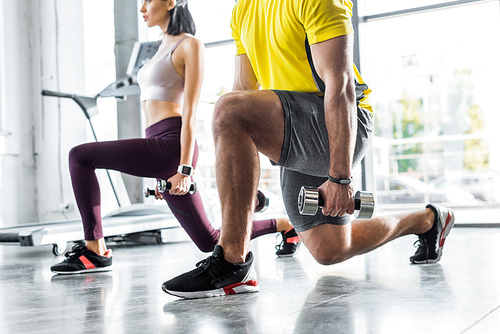 cropped view of sportsman and sportswoman doing lunges with dumbbells in sports center