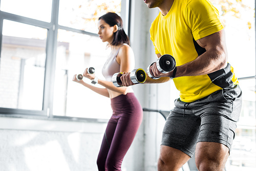 cropped view of sportsman and sportswoman working out with dumbbells in sports center