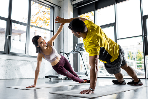 sportsman and smiling sportswoman doing plank and clapping on fitness mats in sports center