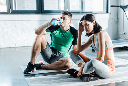 sportsman drinking water and sportswoman sitting in sports center