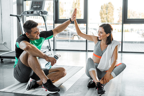 sportsman and sportswoman sitting and giving high five in sports center