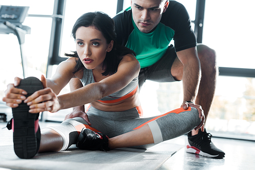 sportswoman stretching and sportsman helping her in sports center