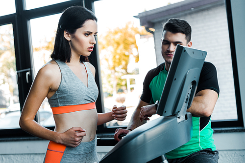 sportswoman running on treadmill and sportsman standing near in sports center