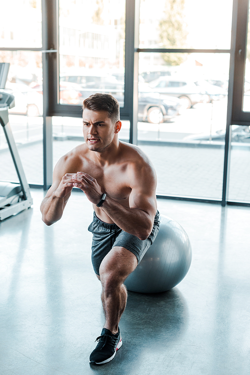 handsome sportsman doing lunges on fitness ball in sports center