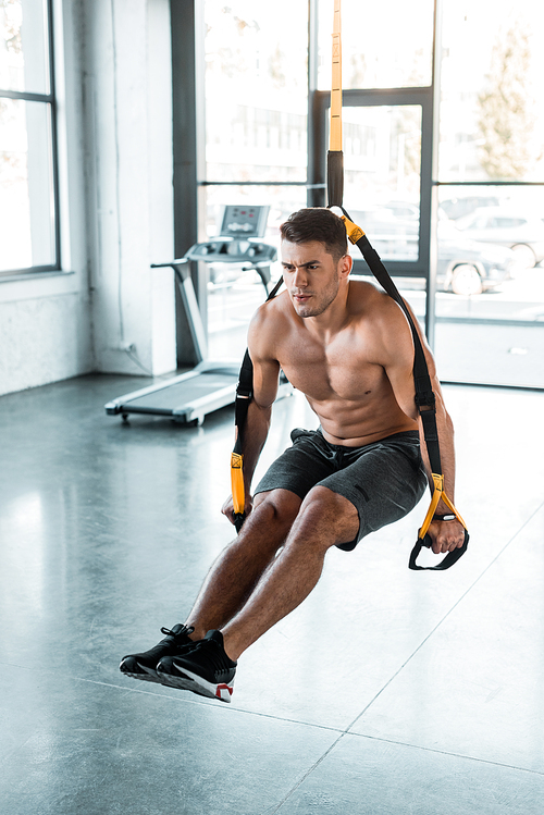 handsome sportsman working out on suspension trainer in sports center