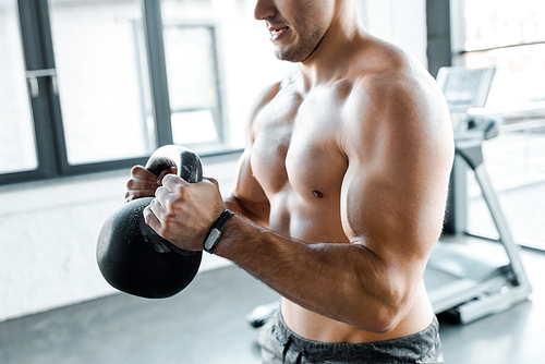 cropped view of shirtless sportsman working out with weight in sports center