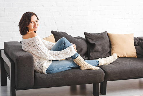 attractive brunette woman sitting on sofa with pillows in cozy living room