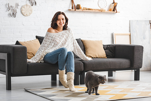beautiful happy woman sitting on sofa with scottish fold cat on floor