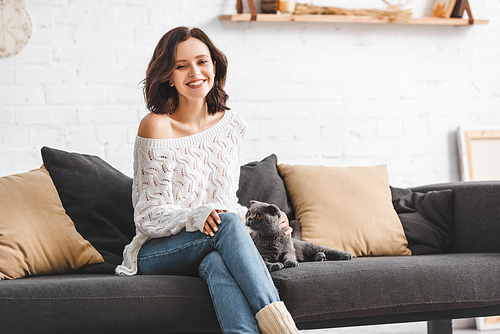 beautiful smiling girl sitting on sofa with scottish fold cat