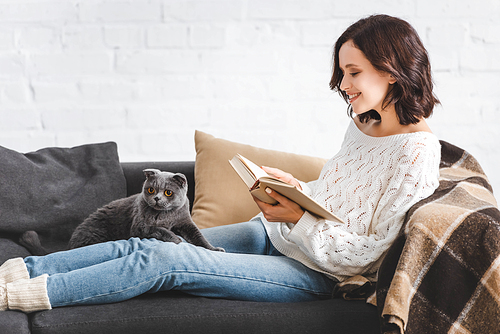 happy girl reading book with scottish fold cat on sofa