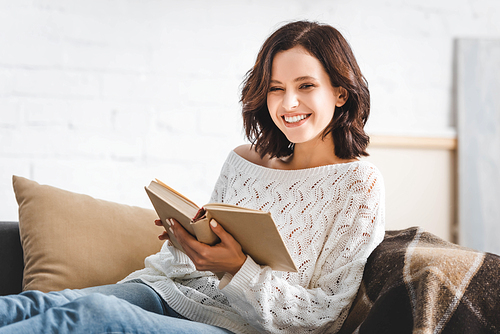 cheerful girl reading book on sofa at home
