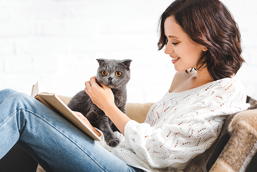 brunette happy woman reading book with scottish fold cat on sofa