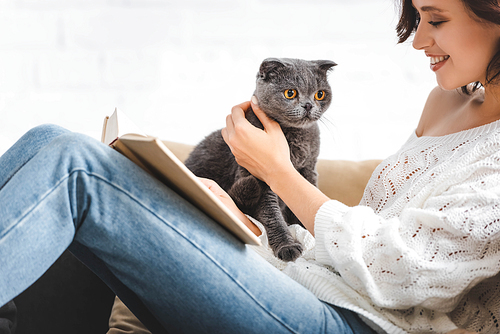 happy girl reading book on sofa with scottish fold cat