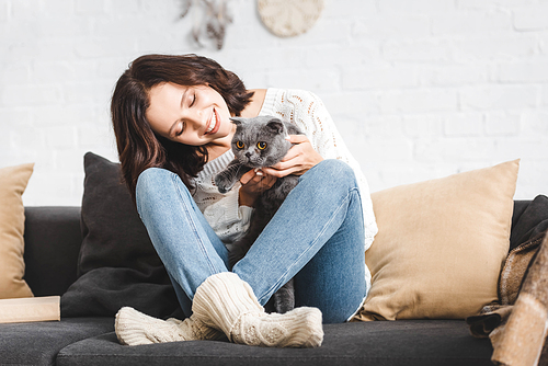 happy woman sitting on sofa with grey scottish fold cat