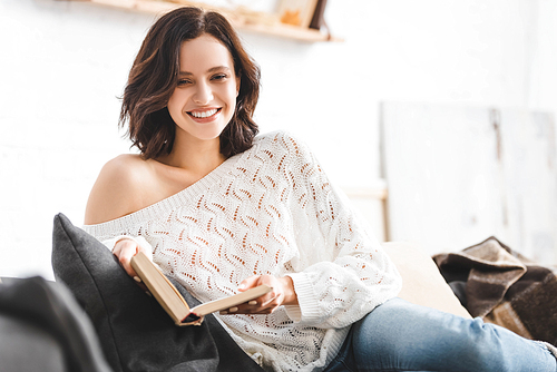 brunette smiling girl reading book on sofa at home