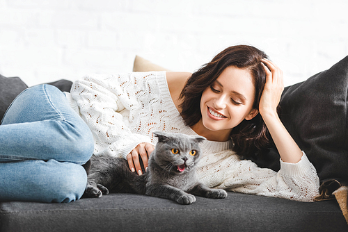 beautiful cheerful woman lying on sofa with scottish fold cat