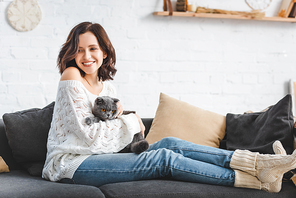 beautiful happy girl sitting on sofa with scottish fold cat