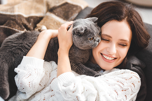 beautiful smiling girl lying on sofa with scottish fold cat