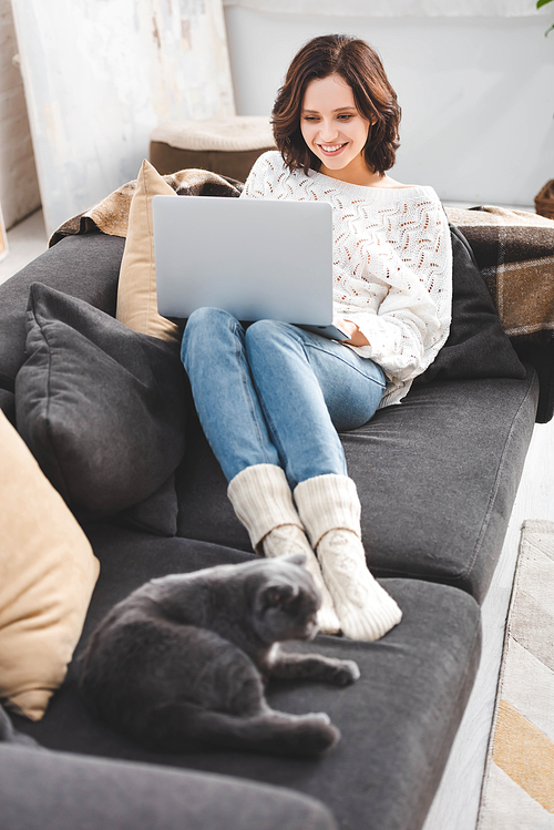 happy woman using laptop with cat on sofa