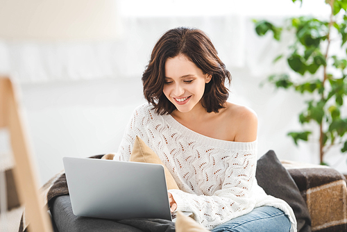 attractive cheerful girl using laptop on sofa in cozy living room