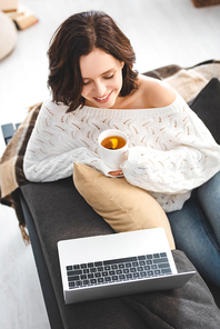 happy girl with cup of tea watching movie on laptop at cozy home
