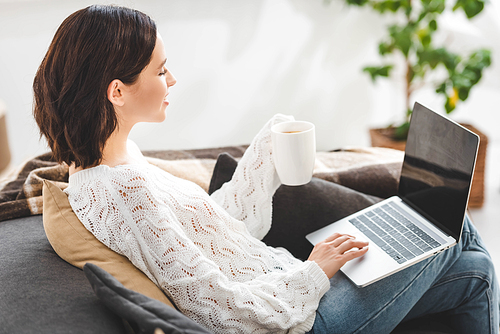 beautiful girl with cup of tea using laptop at cozy home