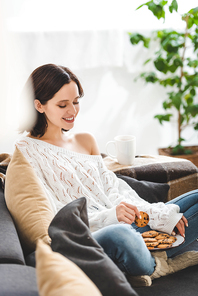 beautiful happy woman sitting on sofa with cookies