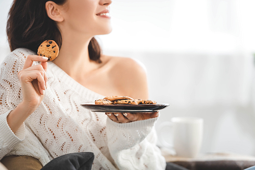 cropped view of happy woman holding plate with cookies