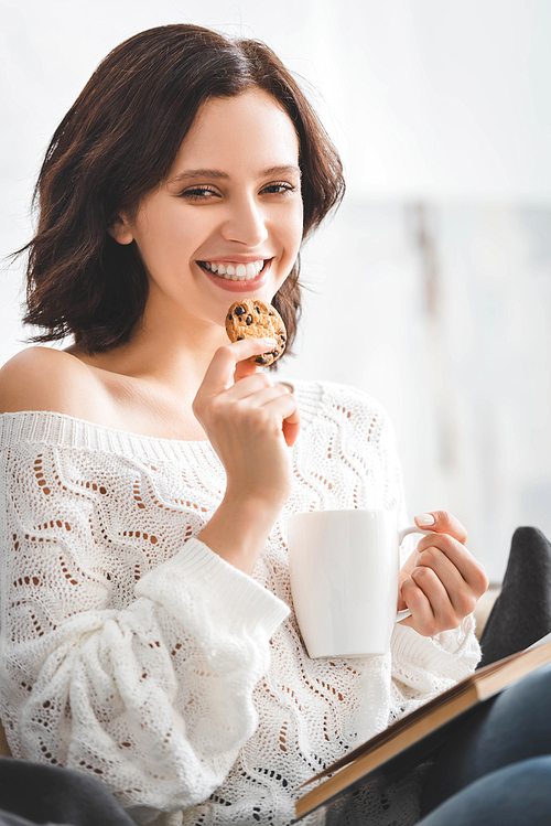 brunette cheerful girl reading book on sofa with coffee and cookies