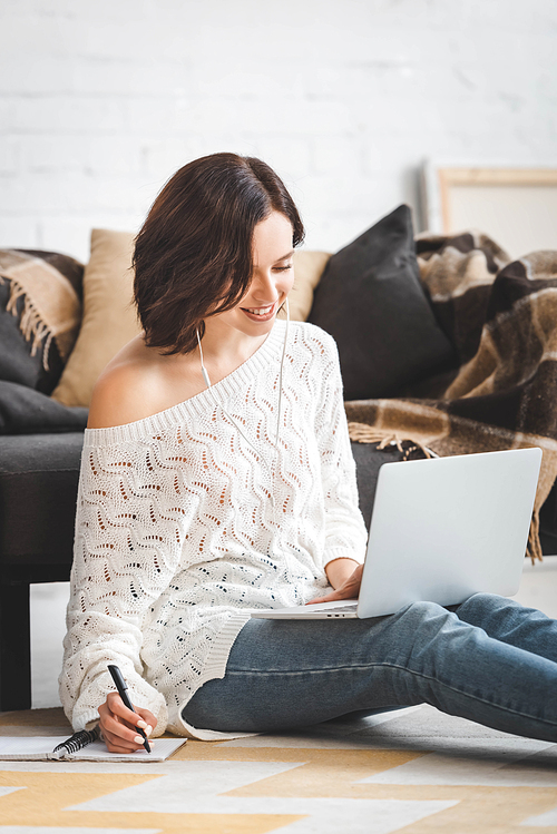 happy young woman with earphones studying online with laptop and notebook at home