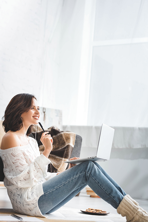 dreamy girl studying online with earphones and laptop on floor