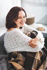 smiling girl in blanket sitting on sofa in cozy living room