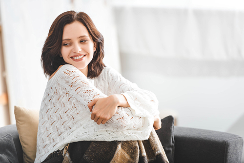 beautiful happy woman with blanket sitting on sofa in cozy living room