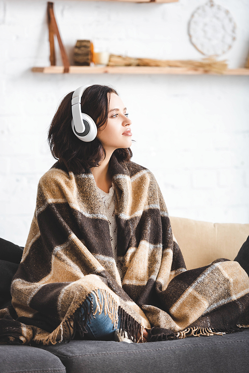 beautiful girl thinking and listening music with headphones while sitting in blanket