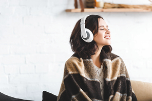 happy woman with closed eyes in blanket listening music with headphones