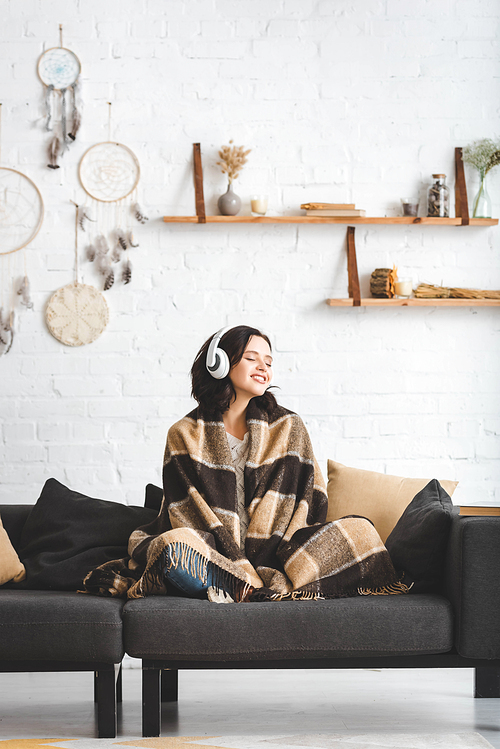 brunette girl with closed eyes in blanket listening music with headphones