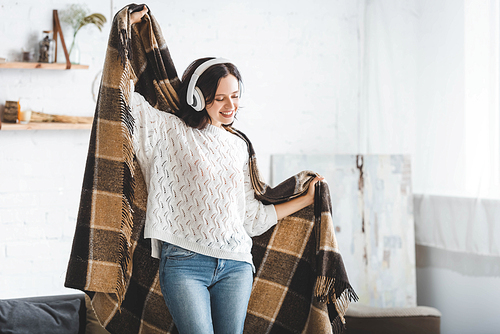 attractive happy woman dancing with blanket while listening music with headphones