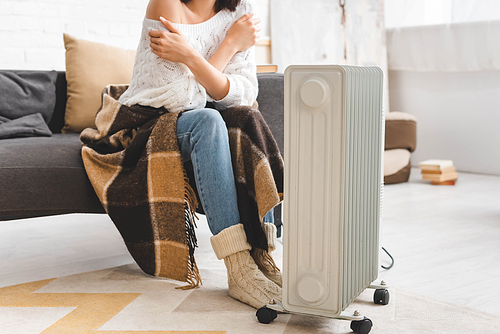 cropped view of woman with blanket warming up with heater in cold room